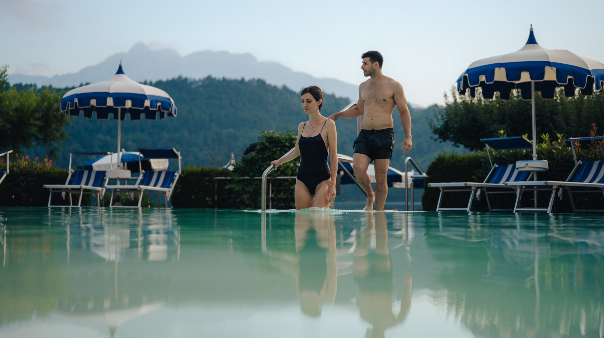 Coppia che entra nella piscina esterna del Parc Hotel Du Lac, con vista sulle montagne del Trentino
