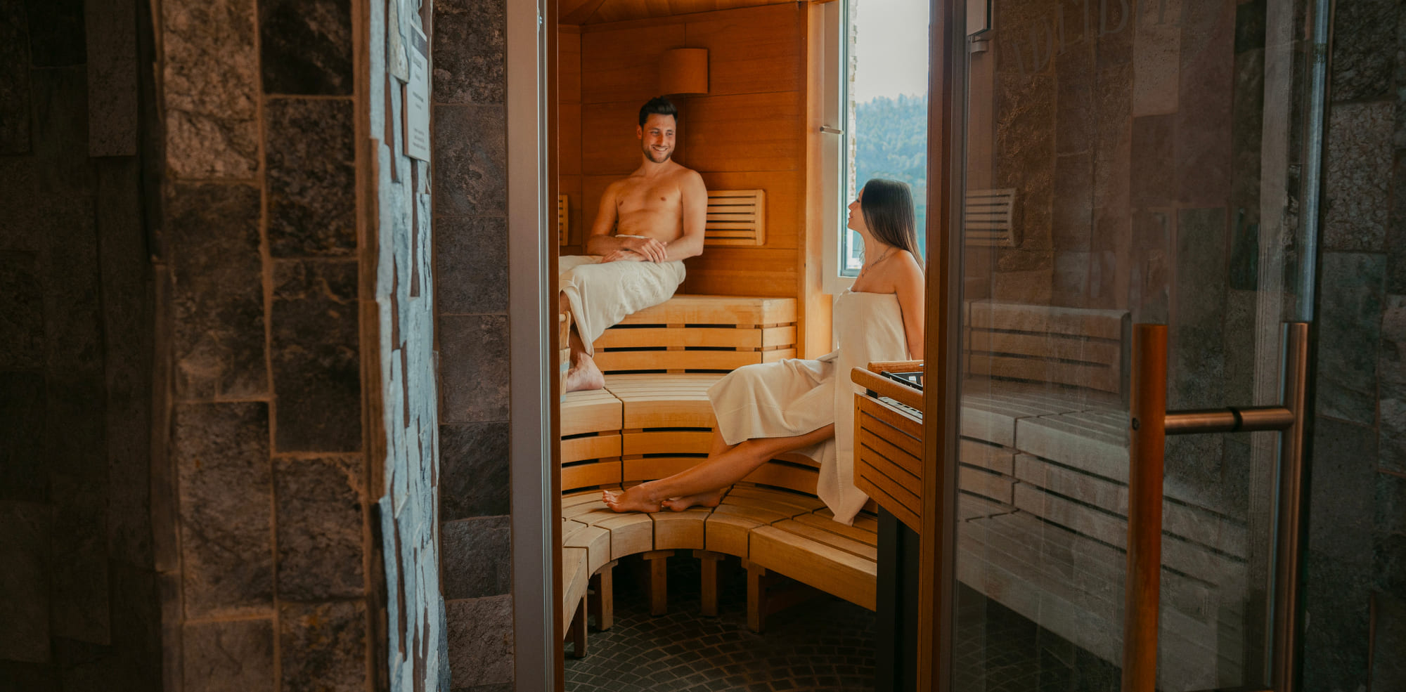 Coppia che si rilassa nella sauna panoramica del Parc Hotel Du Lac con vista sul Lago di Levico