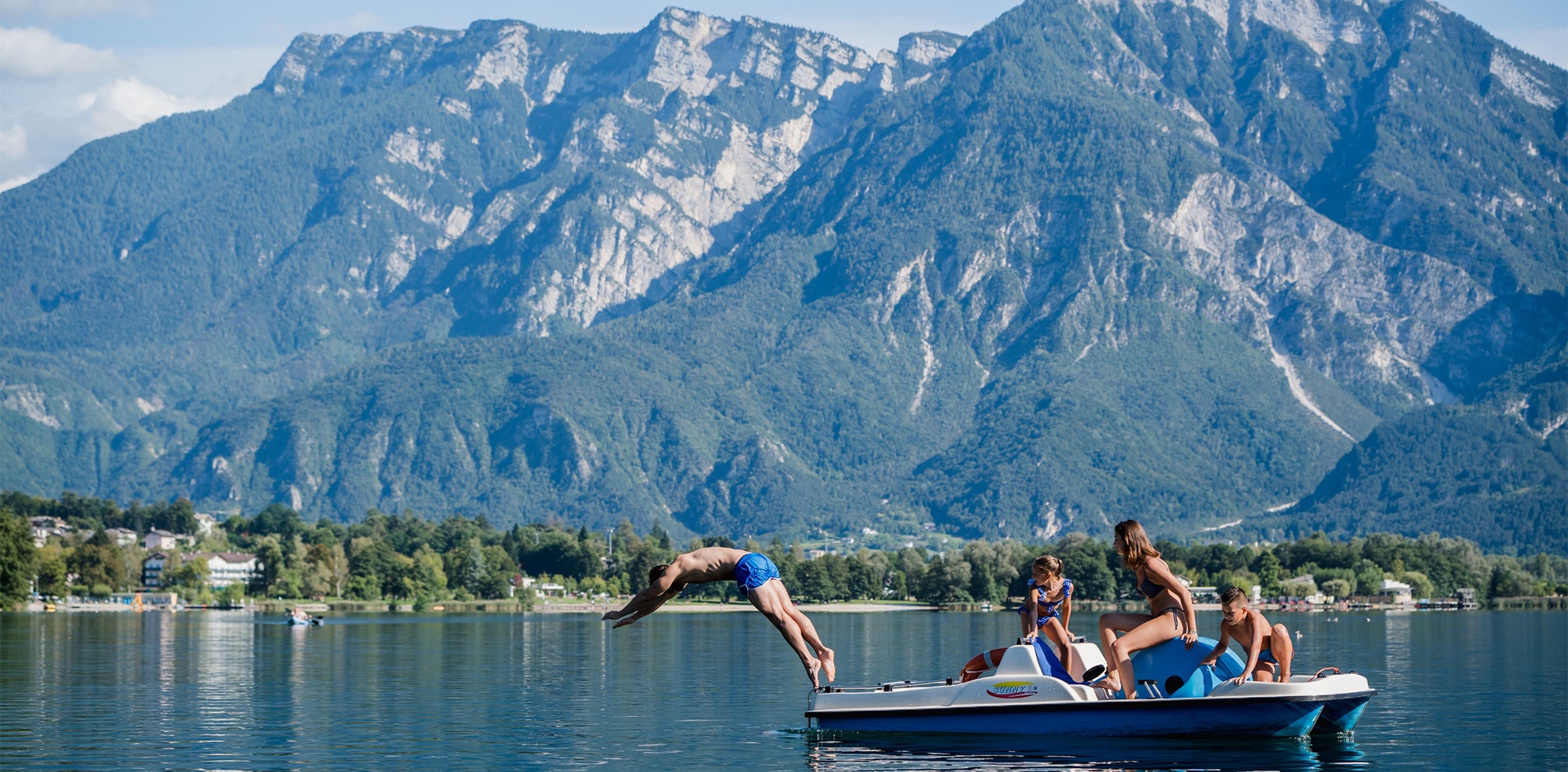 Una famiglia sul pedalò e una persona che si tuffa nel Lago di Levico e vista panoramica