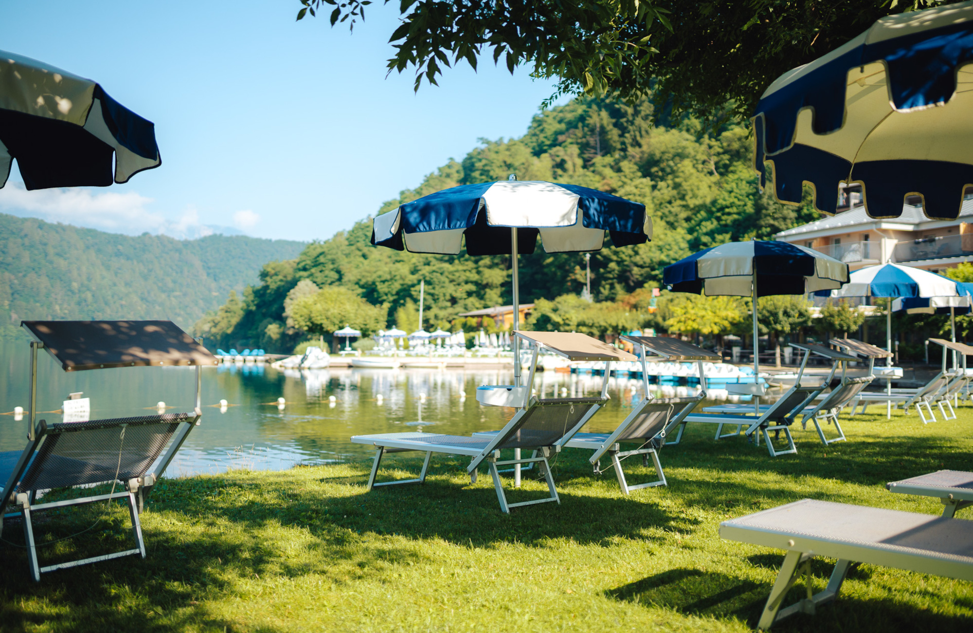 Spiaggia privata con lettini e ombrelloni blu sulla riva del Lago di Levico, al Parc Hotel Du Lac