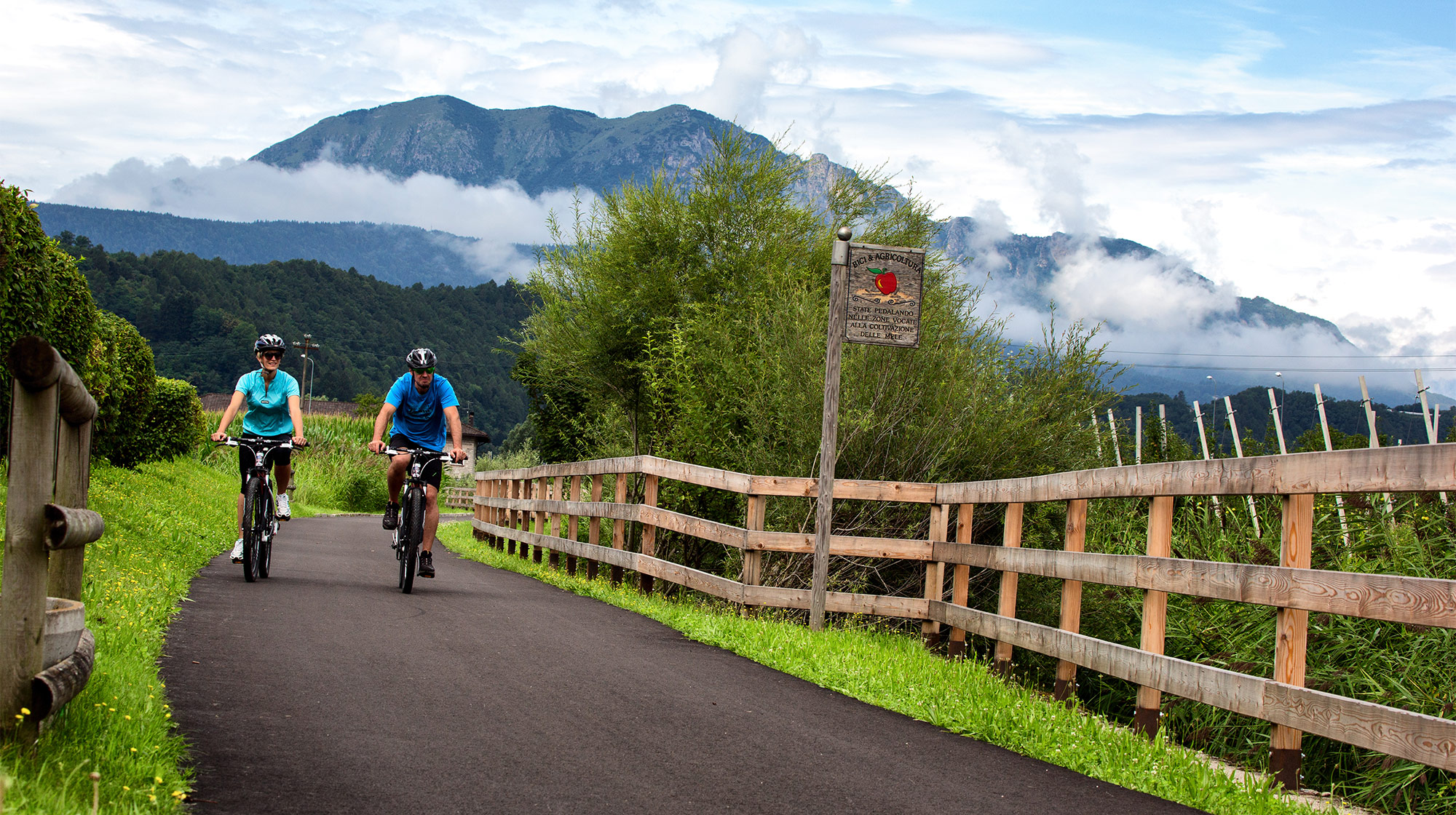 Coppia in bicicletta lungo la pista ciclabile panoramica della Valsugana, tra natura e montagne del Trentino
