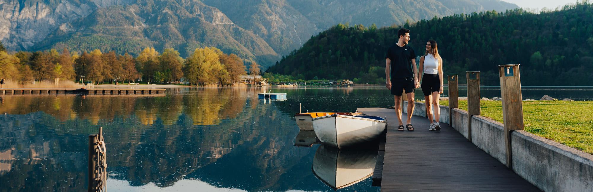 Coppia che passeggia sul pontile del Lago di Levico tra natura e riflessi d’acqua in autunno
