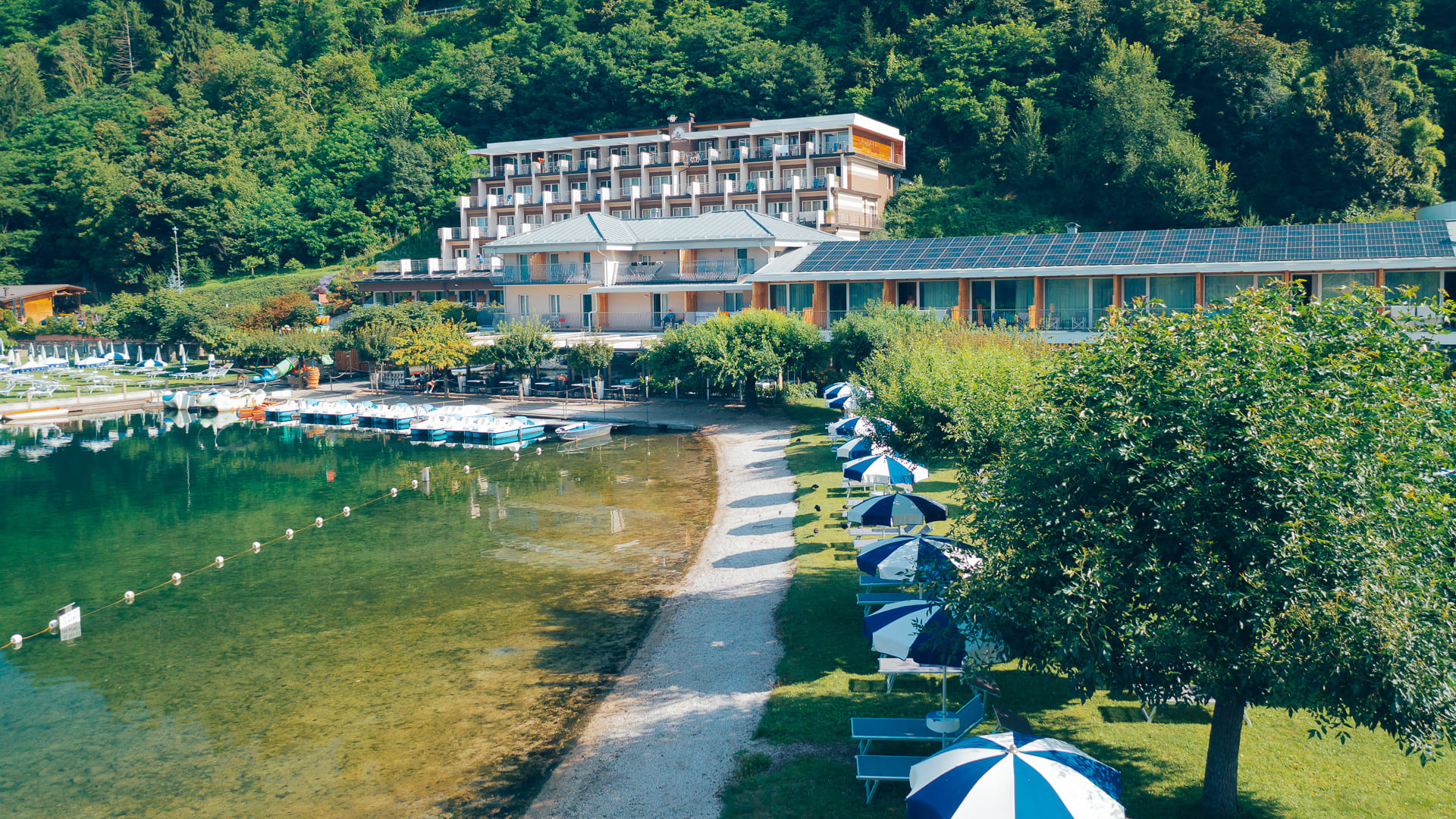 Vista dell’hotel con accesso diretto al lago con spiaggia privata e lettini sull’erba.