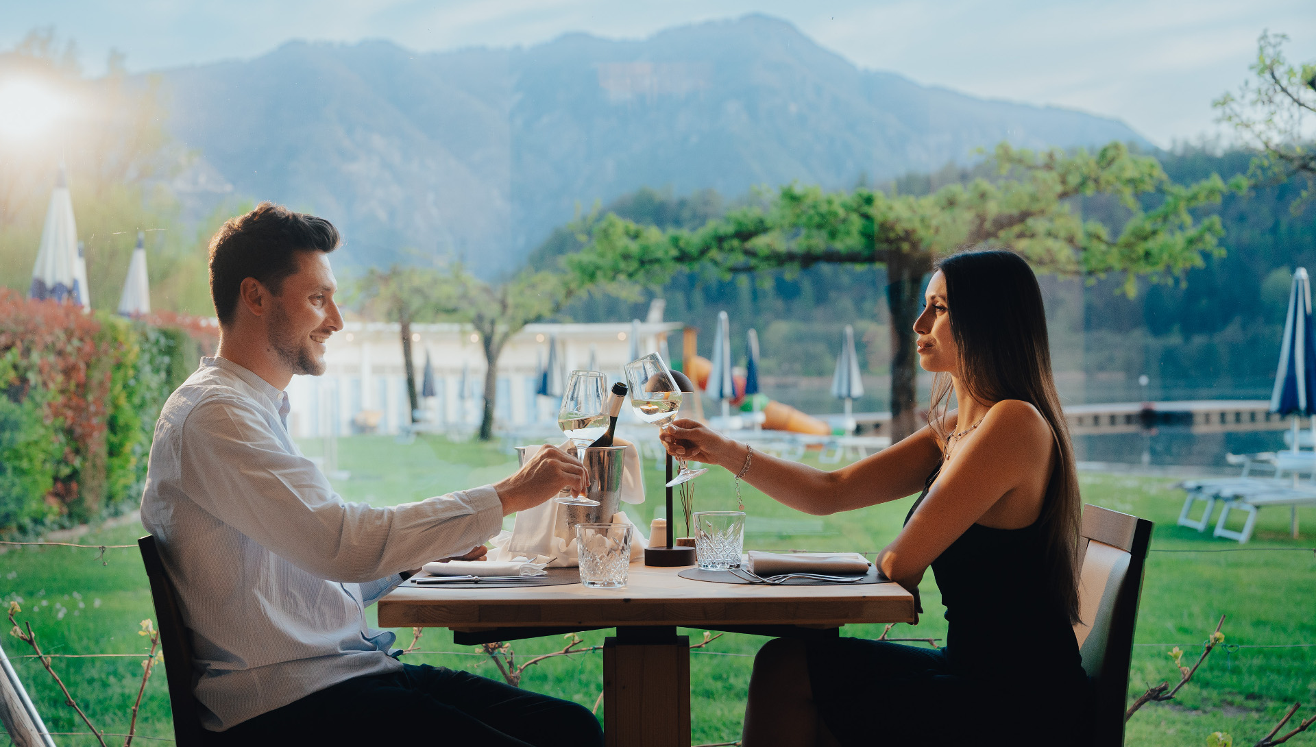 Coppia brinda a cena con vista sul lago e sulle montagne.